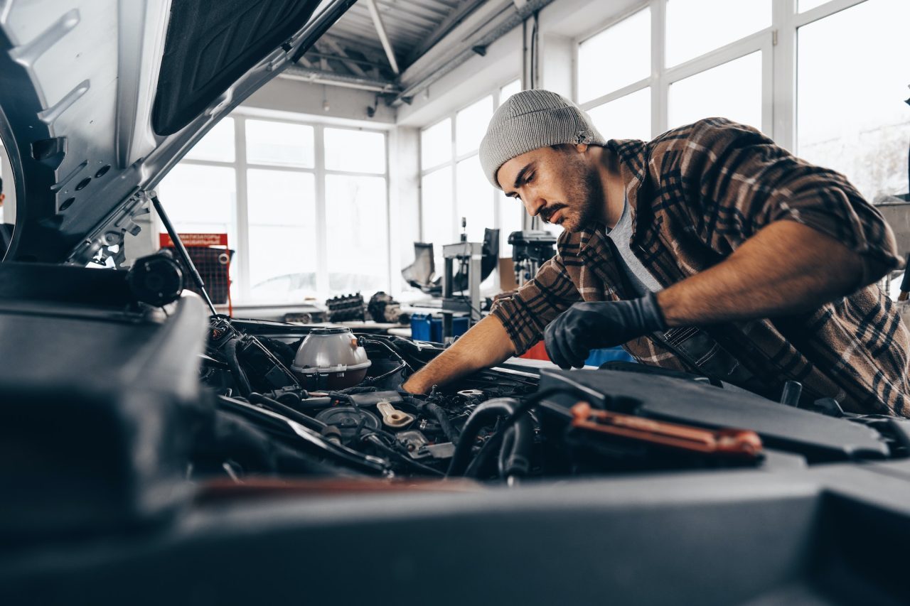 Mechanic repairing a car engine under the open bonnet in a bright workshop