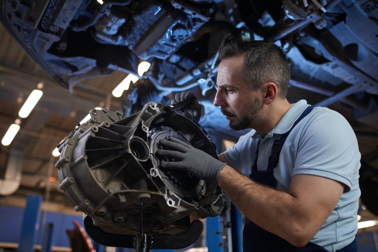 Mechanic inspecting a car gearbox underneath a vehicle on a lift
