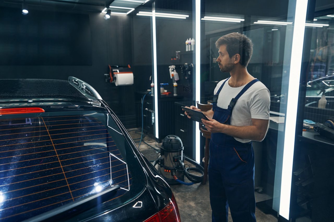 Detailer holding a tablet beside a car in a car detailing bay